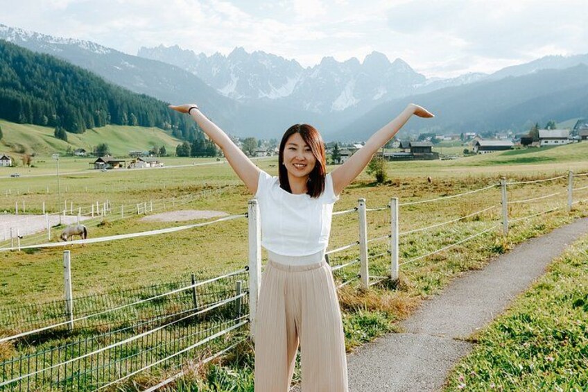 A person standing with arms raised, a rural landscape with mountains in the background, a fence, and a path. 3