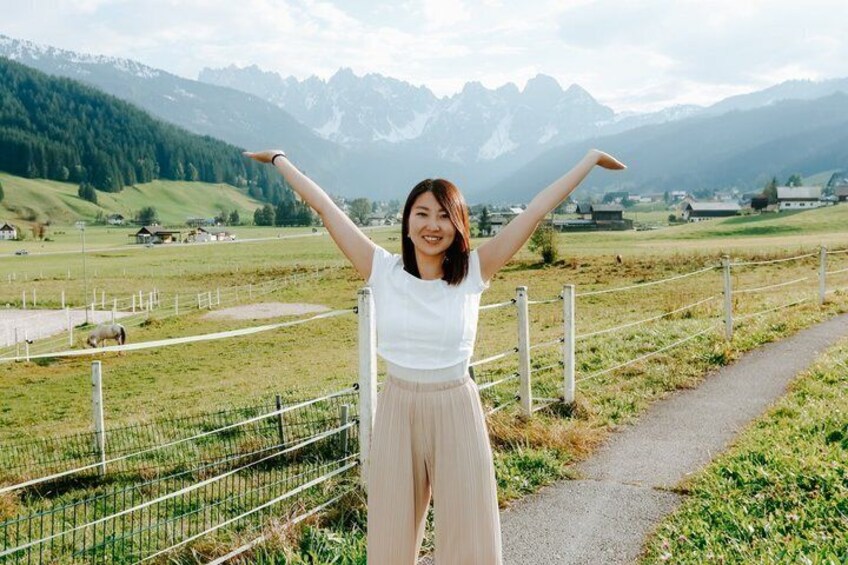 A person standing with arms raised in a rural landscape with mountains in the background. 3