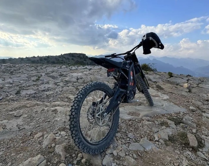 A mountain bike parked on rocky terrain with a mountainous landscape in the background. 1