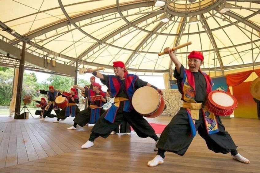 A group performing a traditional dance with drums in a covered outdoor area. 1