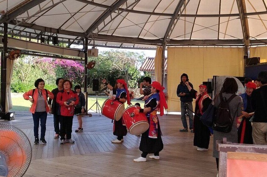 A group of people performing on a stage with musical instruments, under a covered area with a wooden floor. 5
