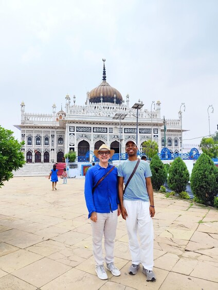 A large white building with intricate designs and a dome, surrounded by greenery and a paved area. 2