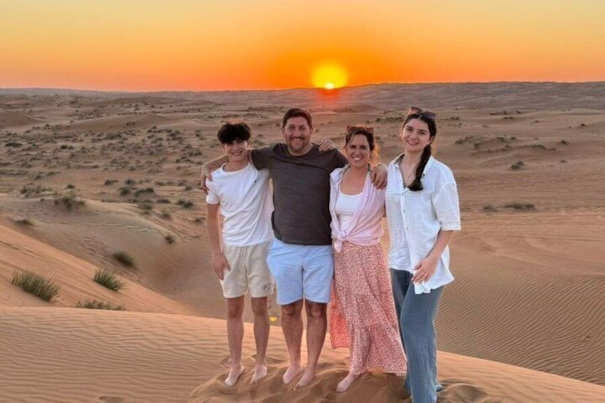 A group of people standing on a sand dune with a sunset in the background. 5