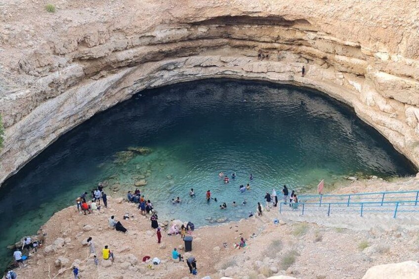 A natural rock formation with a pool of water, surrounded by people. 4