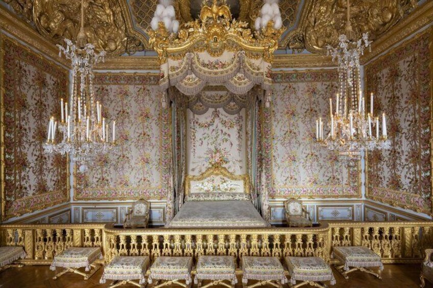 An opulent room with a large bed, ornate chandeliers, and elaborate wall decorations. 4