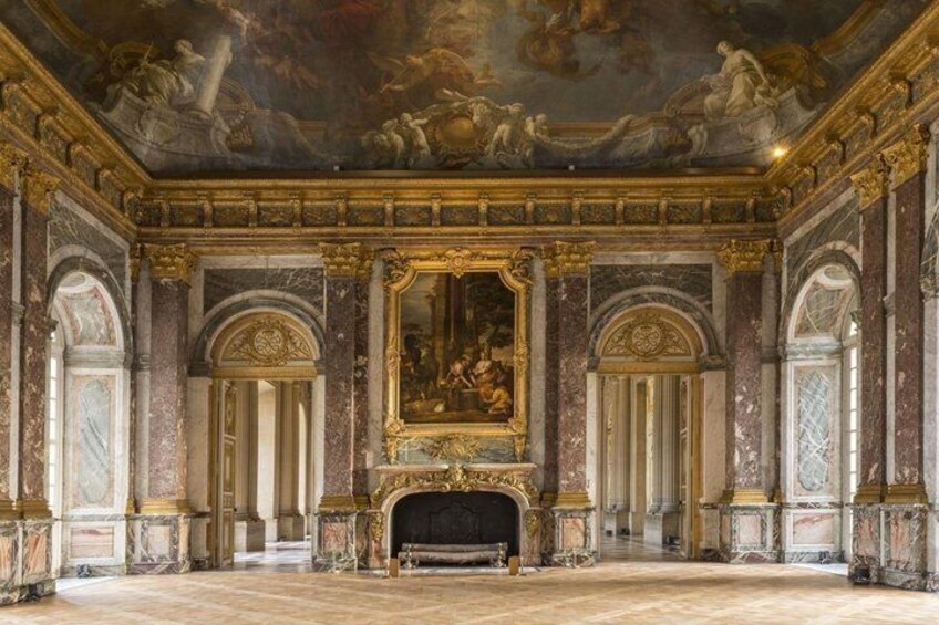 A grand hall with a large fresco, marble columns, and a fireplace. 3