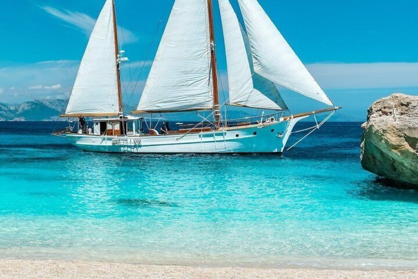 A sailboat with white sails on turquoise water near a rocky shore. 3