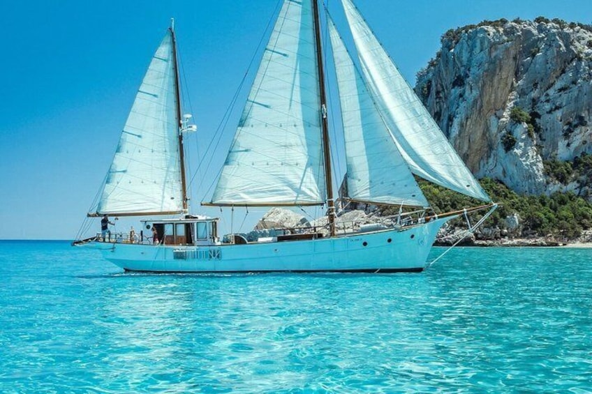 A sailboat on turquoise water with a rocky coastline in the background. 4