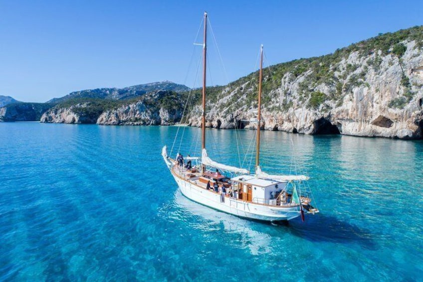A sailboat on clear turquoise water with rocky cliffs in the background. 1