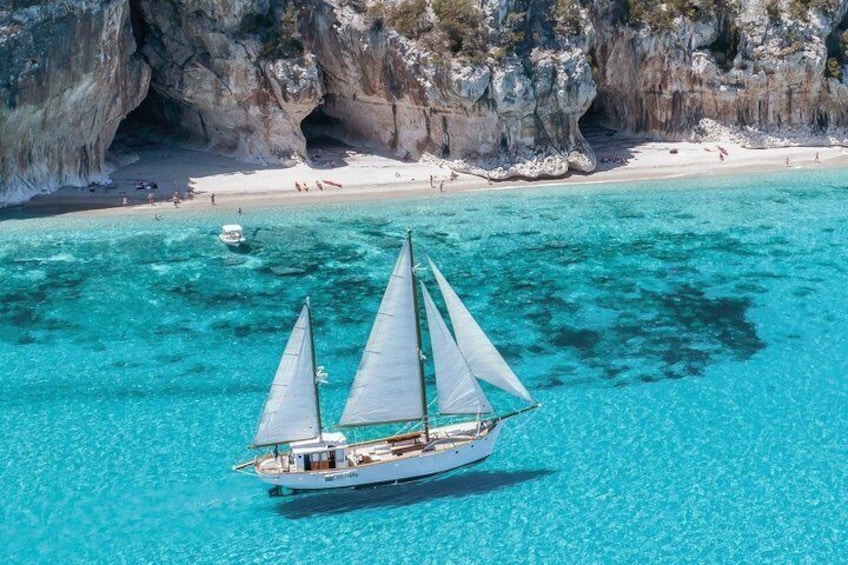 A sailboat on turquoise waters with a rocky coastline and a sandy beach in the background. 5