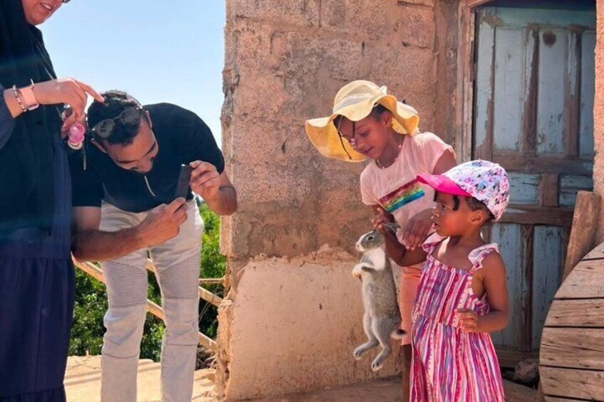 A group of people interacting with a goat near a rustic building. 5