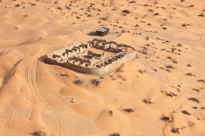 A desert landscape with sand dunes and a small, square-shaped structure with a flat roof, possibly a ruin or historical site. 3