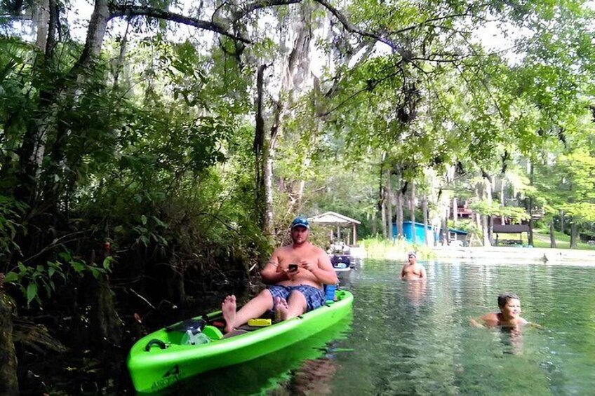 A person in a green kayak on a calm body of water surrounded by dense trees. 5