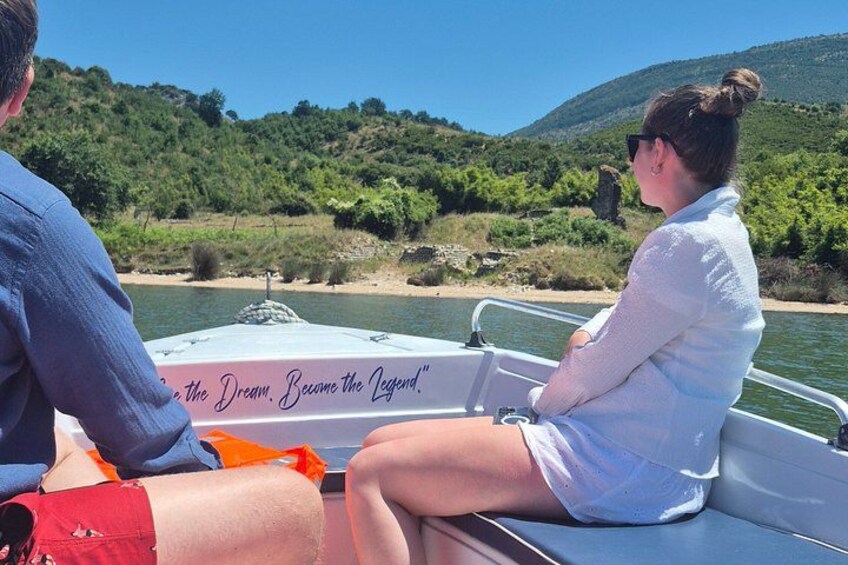 Two people on a boat with a river and green hills in the background. 2