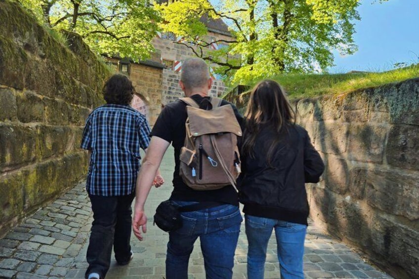 Three people walking on a cobblestone path beside a stone wall. 2