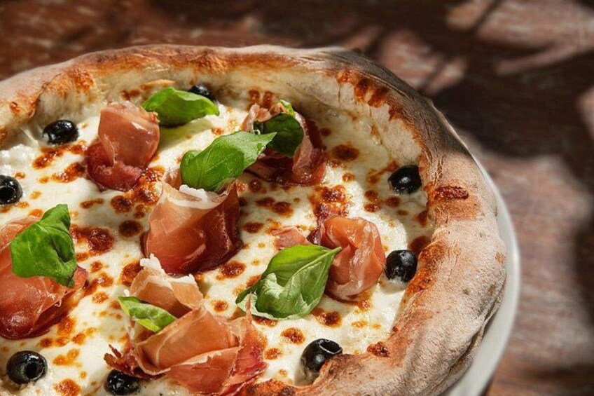Pizza met zwarte olijven, basilicumblaadjes en parmaham op een houten tafel. 5