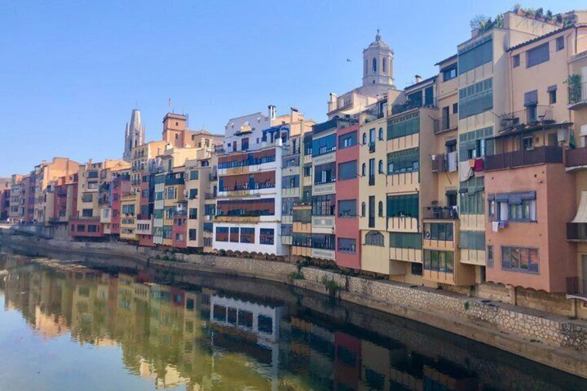A river reflecting colorful buildings, a white boat, and a bell tower. 1