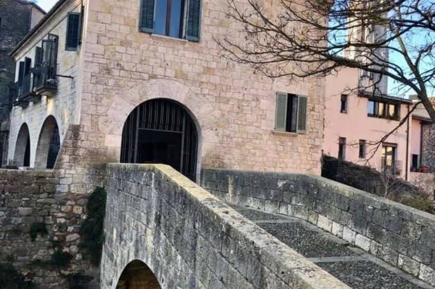 A stone bridge with arches, a pink building with a window, and a tree. 2