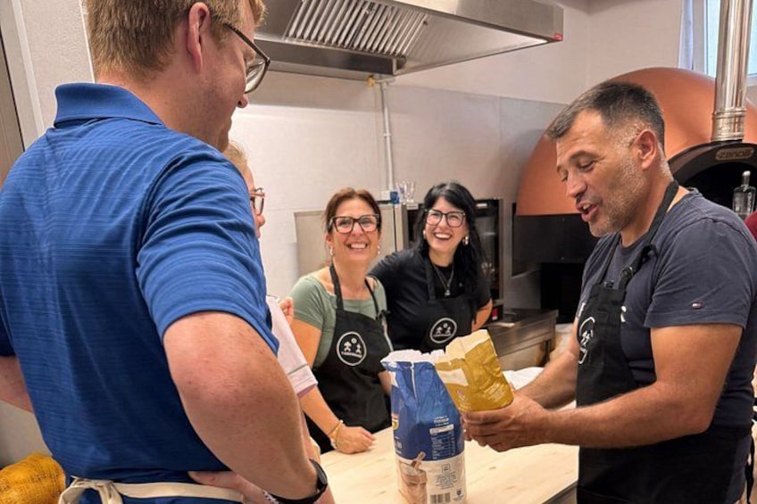 A group of people in a kitchen, one person handing over a bag to another. 1