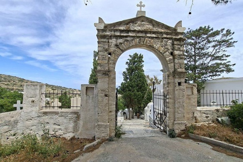 A stone archway with a cross on top, leading to a cemetery with white crosses and a fence. 2