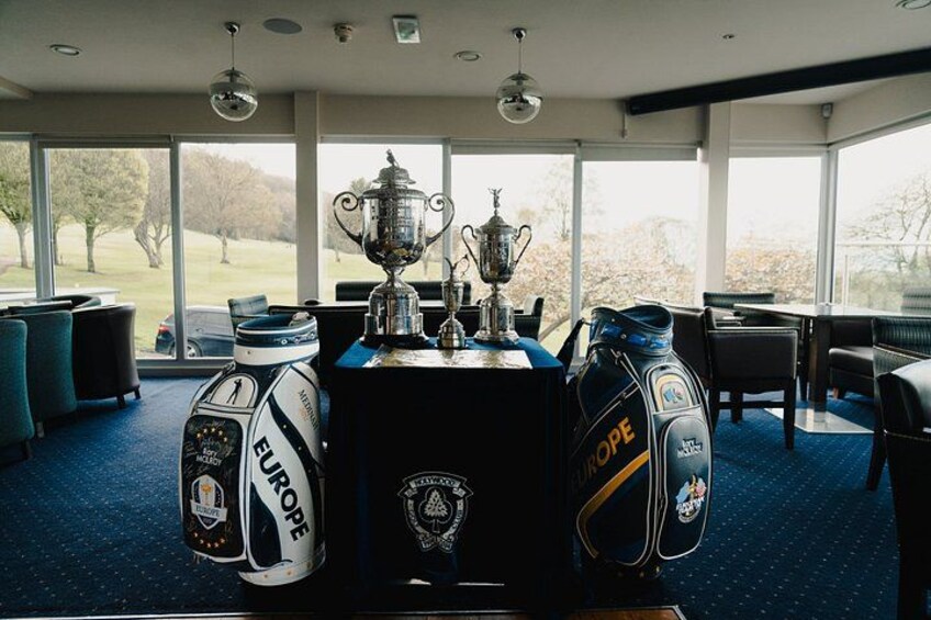 A golf course clubhouse with a trophy on a table, golf bags, and a view of the golf course. 5