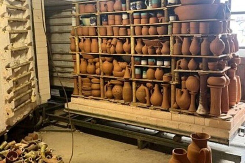 A pottery workshop with shelves of various clay pots and pottery wheels. 1