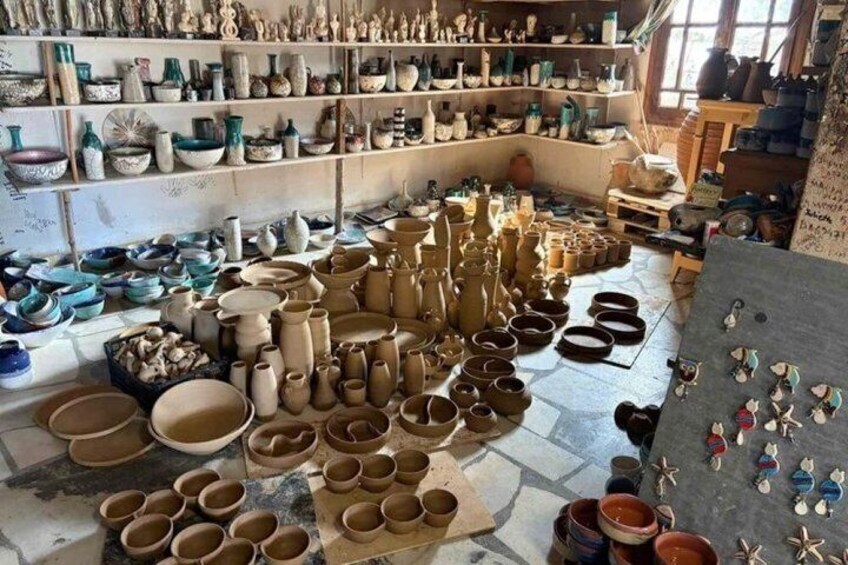 A pottery workshop with shelves of finished pottery and numerous clay pots and bowls on the floor. 5
