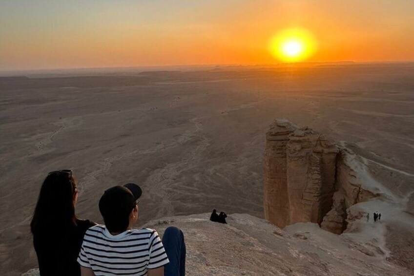 A desert landscape with a sunset, a rock formation, and people observing the view. 2