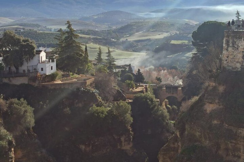 A white building on a cliff, a valley with trees, and a distant mountain range. 4