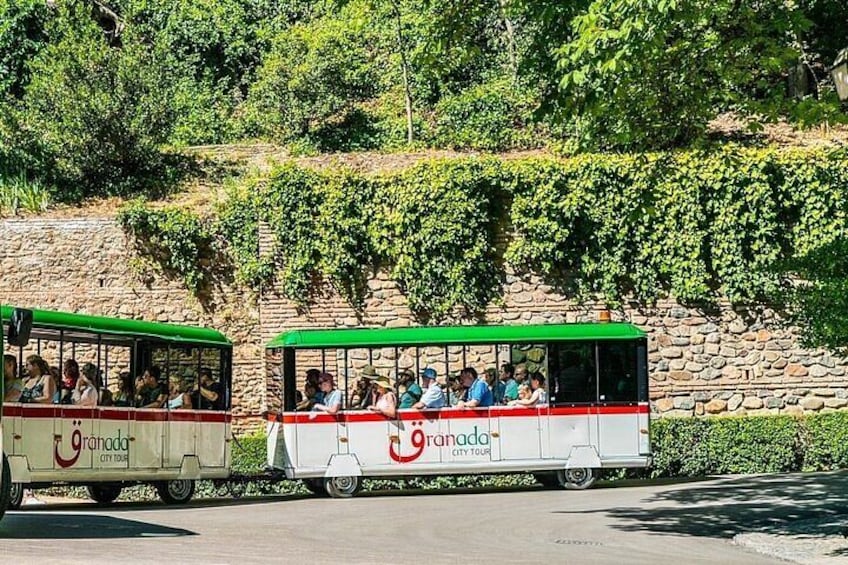 Two city tour vehicles with passengers, parked on a road with a stone wall and greenery in the background. 3