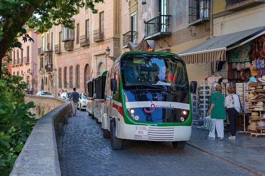 A green and white bus on a cobblestone street with people shopping at a market. 1