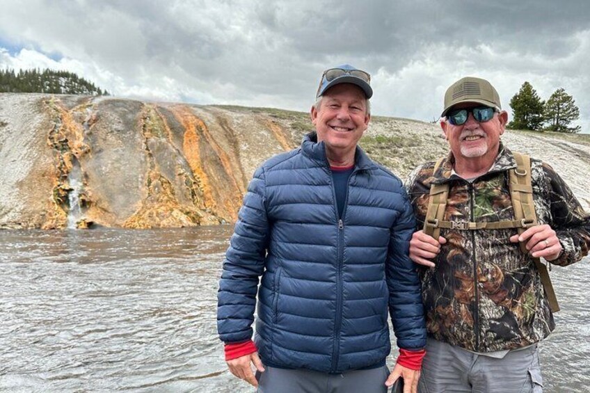 Two people standing by a geothermal area with mineral deposits and a water body. 5