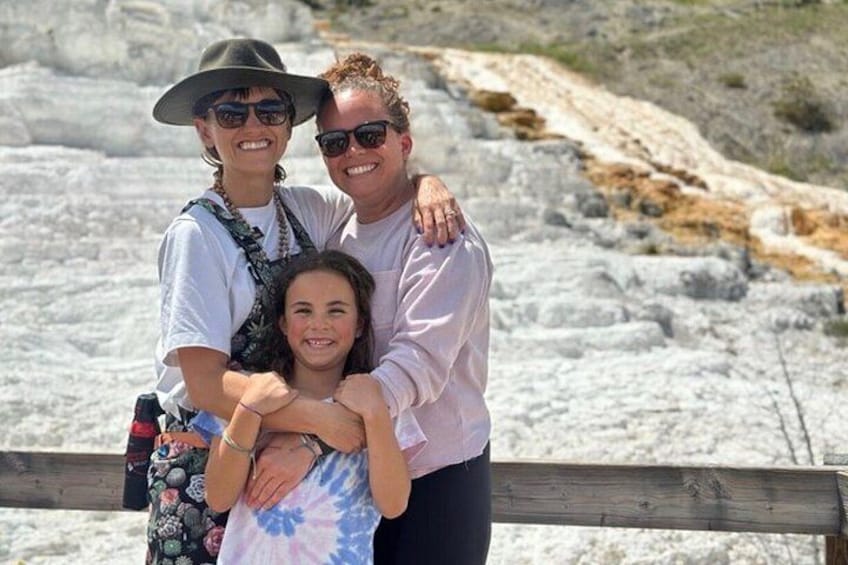 A family of three standing on a rocky terrain with a wooden fence in the foreground. 5