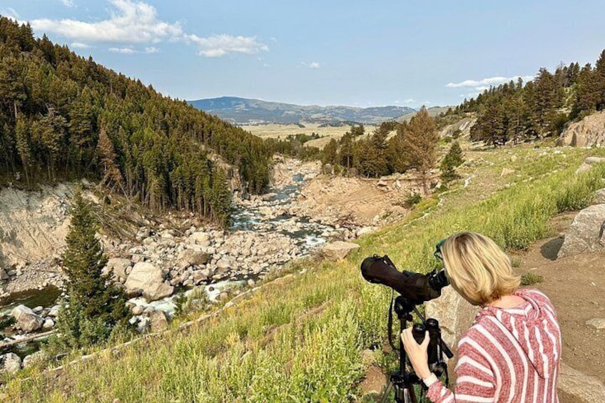 A person with a camera on a tripod, overlooking a river with surrounding forest and hills. 4