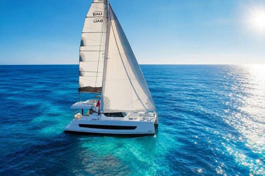A sailboat with a white hull and sails, sailing on clear blue waters. 3