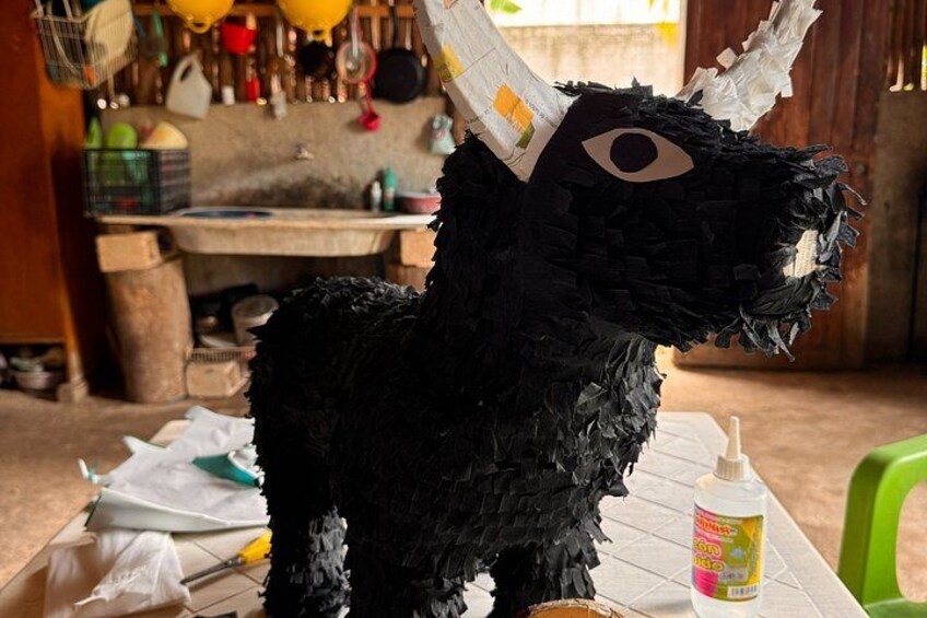 A black piñata with a face, a green chair, and a table with a bottle of glue. 2