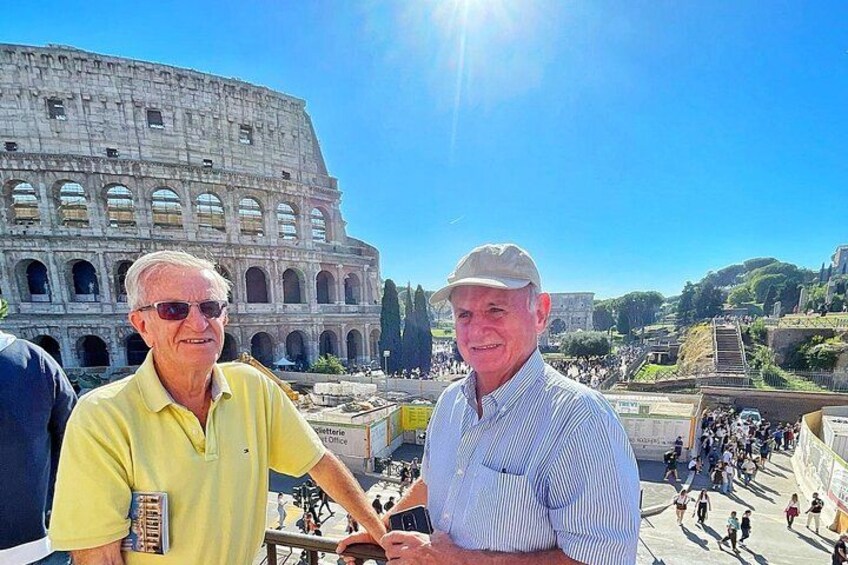 To personer står foran Colosseum, turister i baggrunden. 5