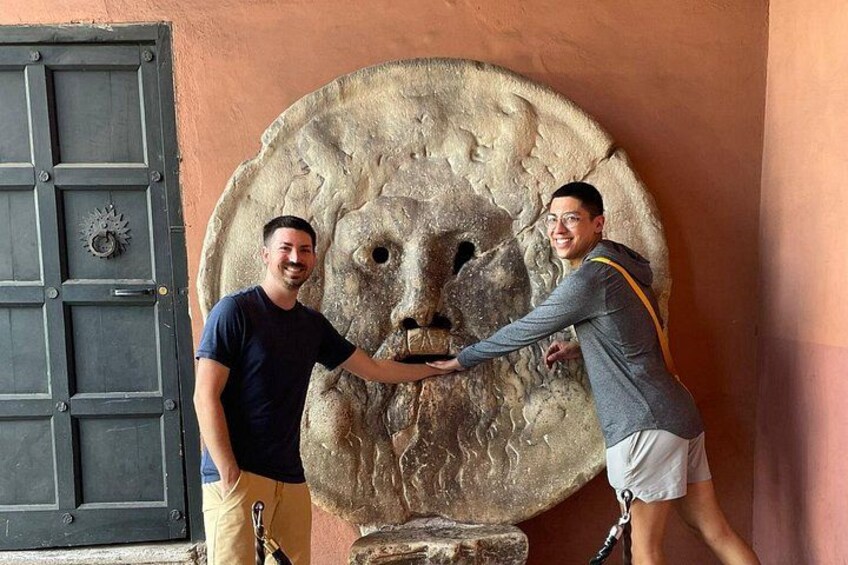 Two people interacting with a large stone face sculpture. 2
