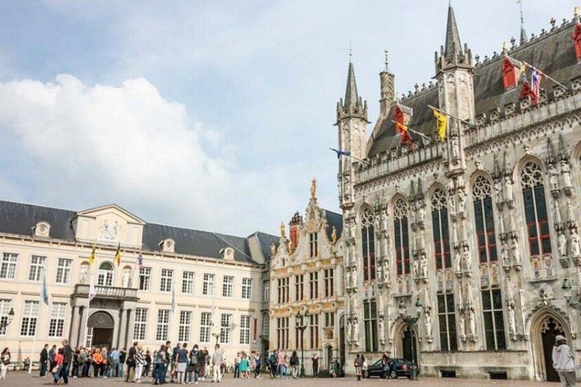 A historic building with intricate architecture, a large open square, and flags. 2