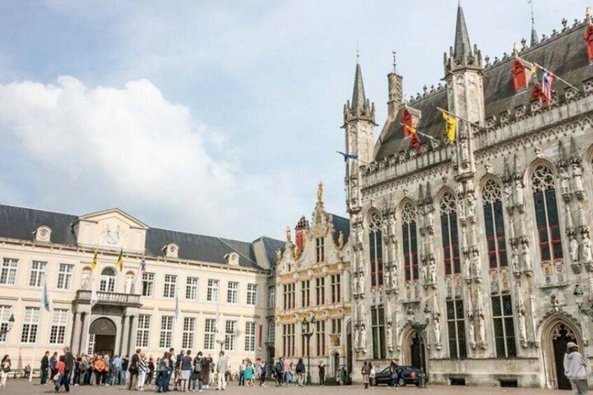 A historic building with ornate architecture, a large open square, and flags. 3