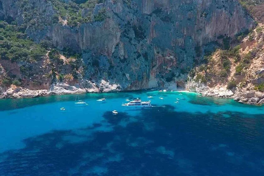 A coastal area with clear blue waters, rocky cliffs, and several boats anchored near the shore. 2