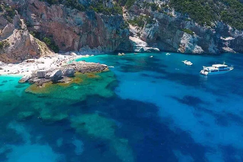 A coastal landscape with clear turquoise waters, rocky outcrops, and boats. 1