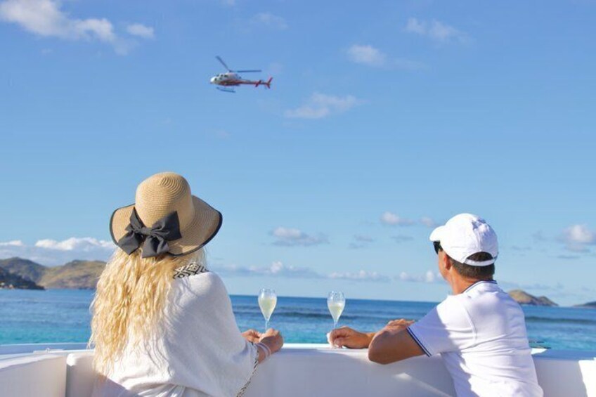 Two people on a boat, a helicopter in the sky, and a clear blue sea. 3