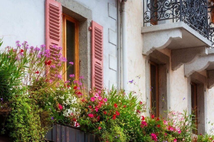 A building with pink shutters, a balcony with wrought iron railings, and a variety of flowering plants. 5