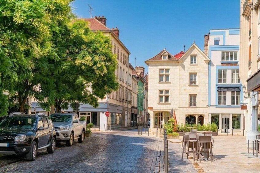 A cobblestone street lined with historic buildings, parked cars, and outdoor seating. 1