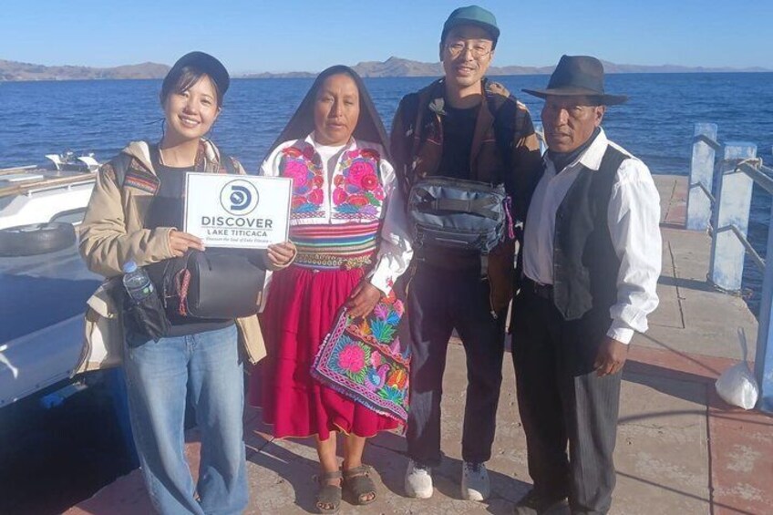 A group of people standing on a dock with a body of water and mountains in the background. 4
