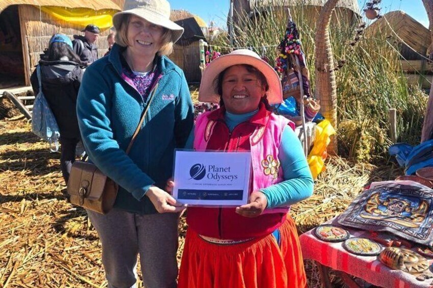 Two people holding a certificate at an outdoor event with a table displaying food and decorations. 2