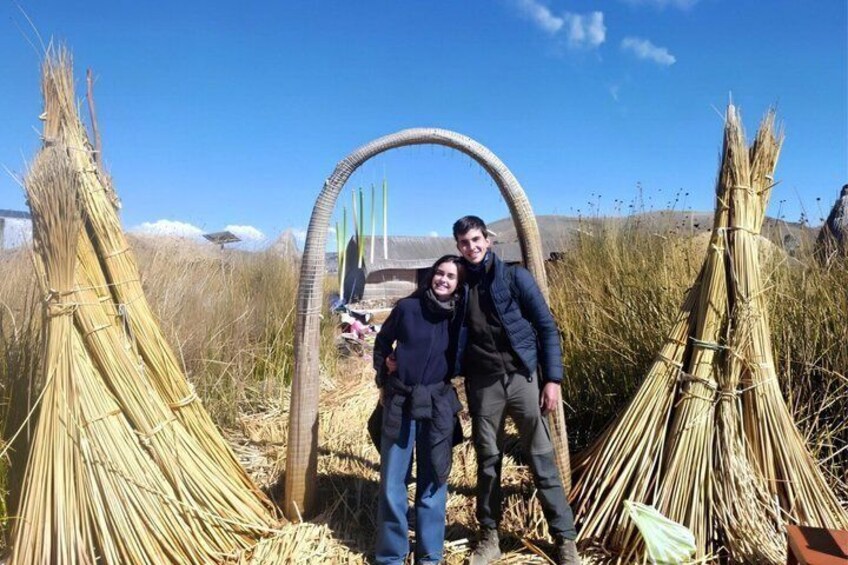 Two people standing in a field with straw structures and a large circular frame. 1