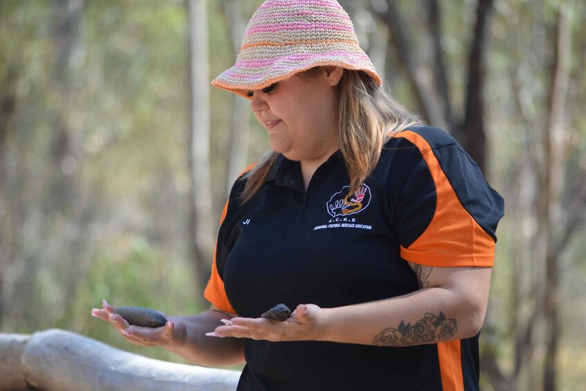 A person wearing a black and orange shirt with a logo, holding two rocks. 3