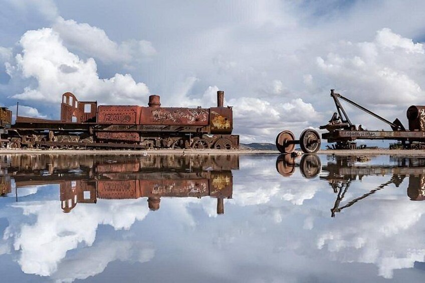 A rusted train and crane by a calm body of water with reflections. 3
